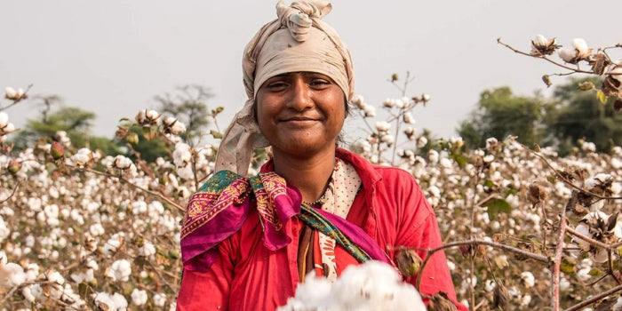 Smiling woman in a cotton field, wearing a red shirt and headscarf.