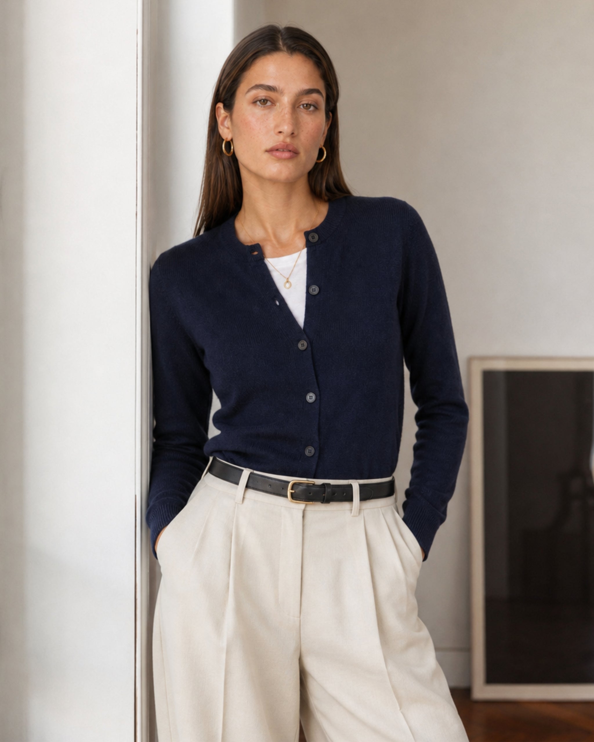 Woman in a navy merino cardigan and cream pleated trousers indoors
