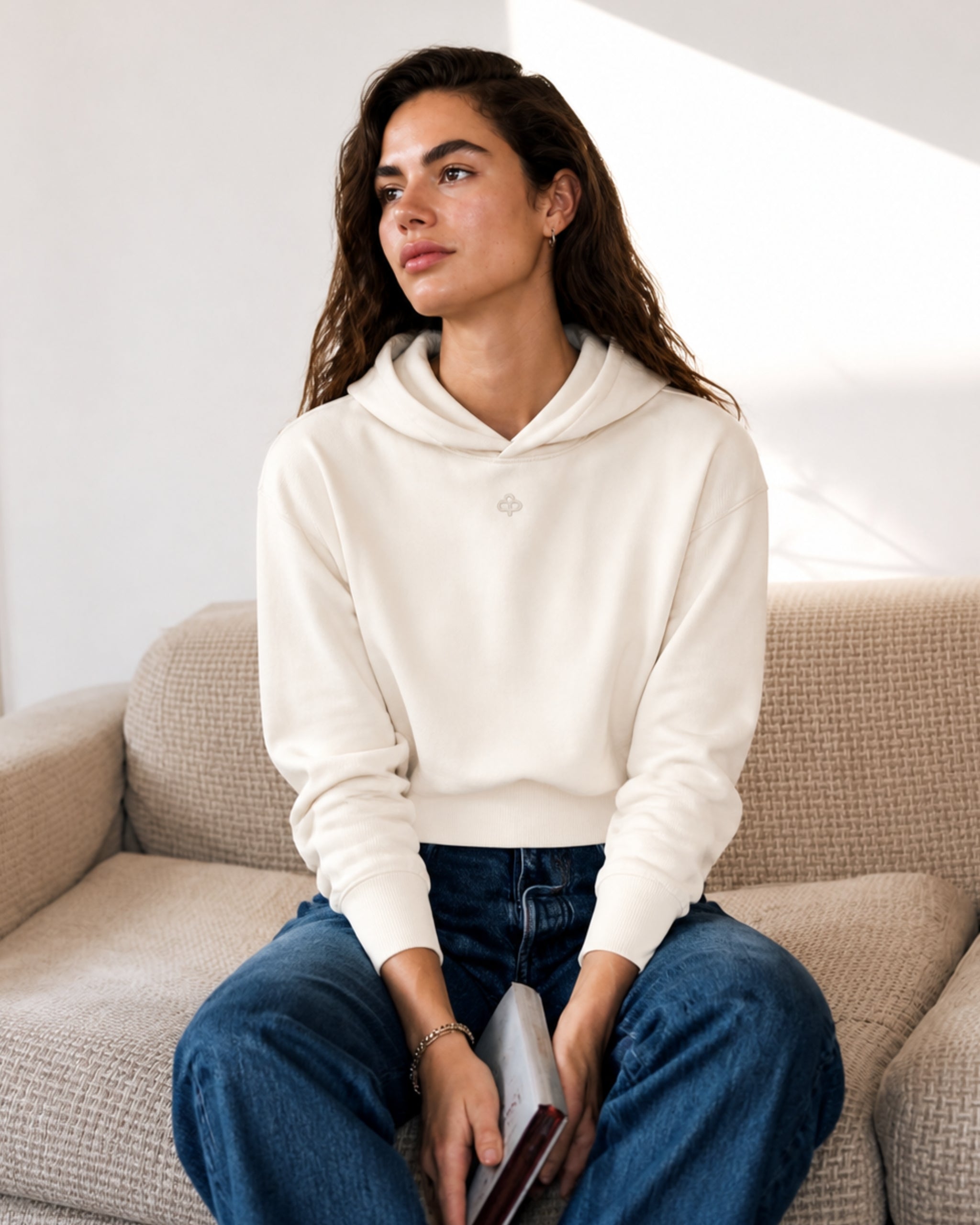Woman in an off-white cotton hoodie and blue jeans seated in an armchair