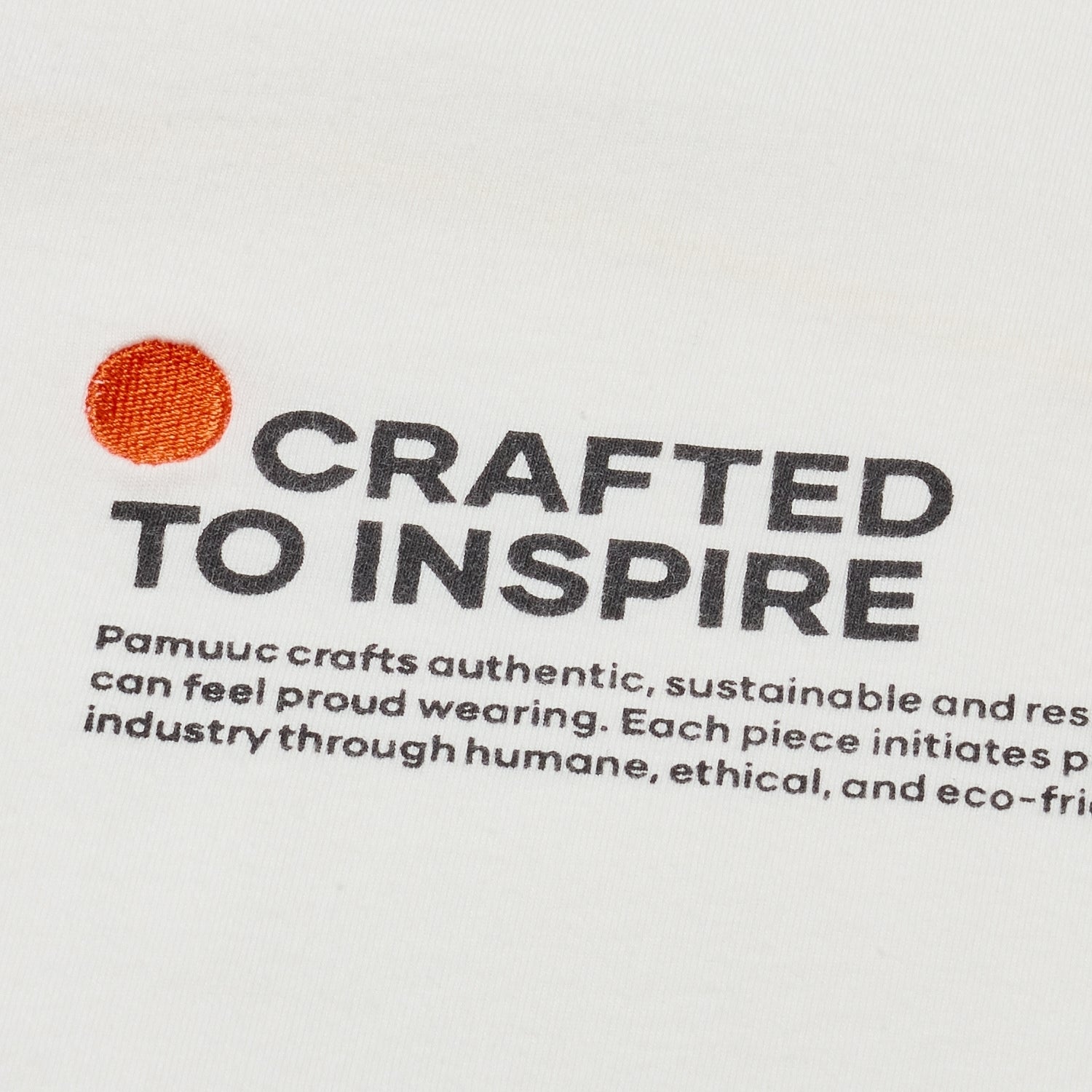 Close-up of 'CRAFTED TO INSPIRE' text and orange logo dot on white fabric