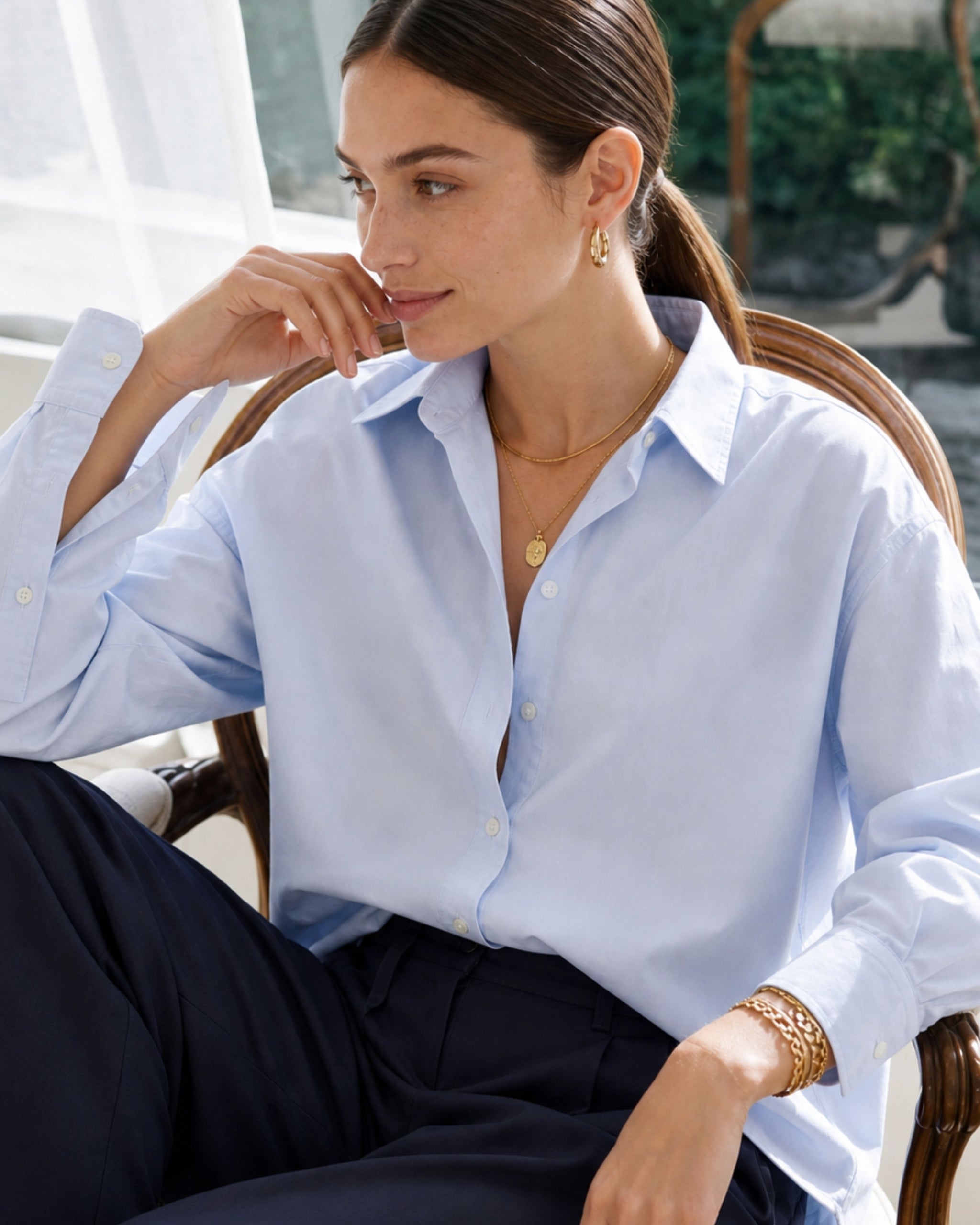 Woman in a light blue poplin shirt seated by a sunlit window