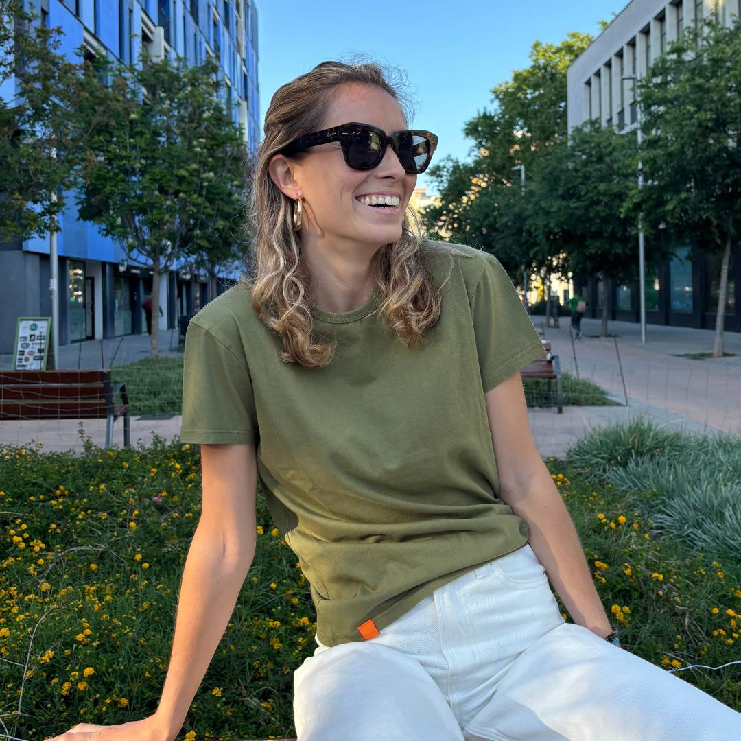 Women wearing a khaki t-shirt sitting on a bench with a street background.